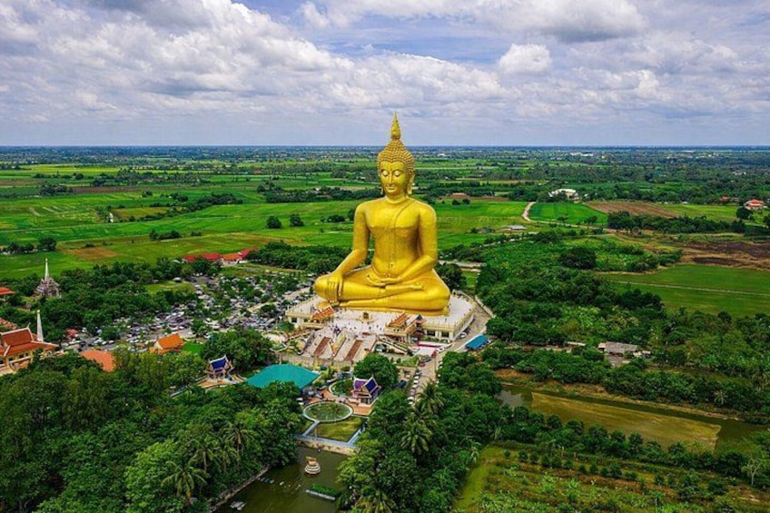 A large golden Buddha statue surrounded by lush greenery and a temple complex. 1