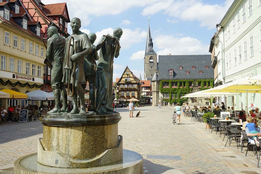 A statue of three figures on a pedestal in a cobblestone square with buildings and a church in the background. 1