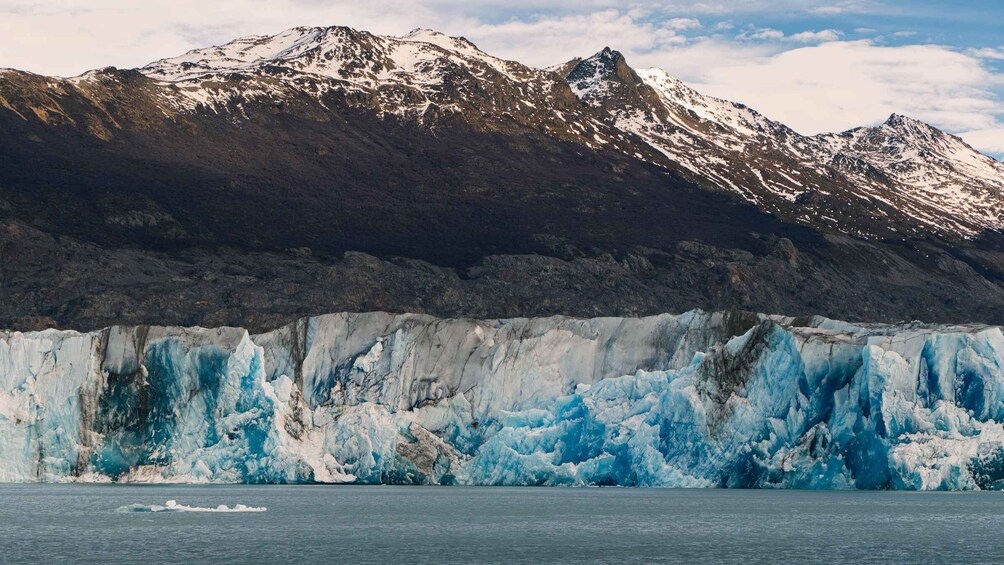 A glacier with a boat in the foreground and mountains in the background. 3
