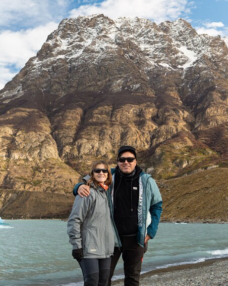 Two people standing by a lake with a mountainous backdrop. 4
