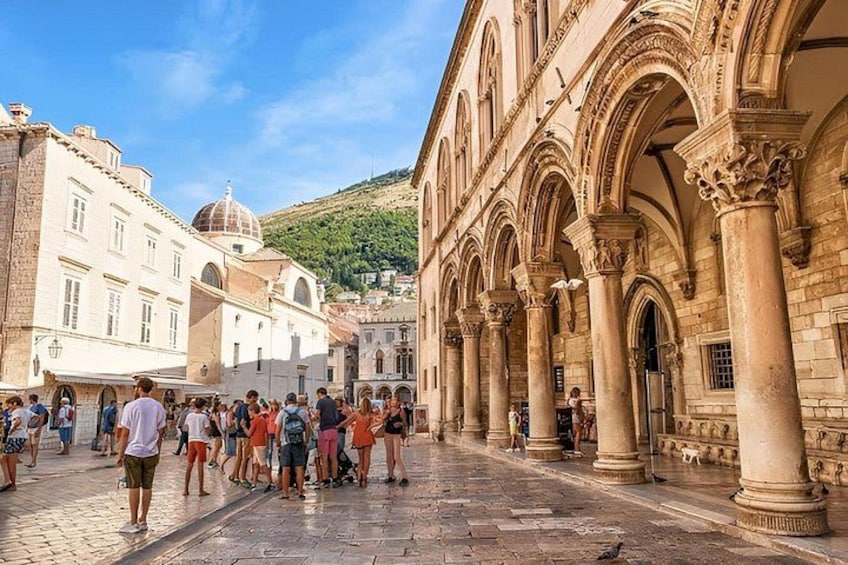A historic square with people, a building with arches, and a dome in the background. 1