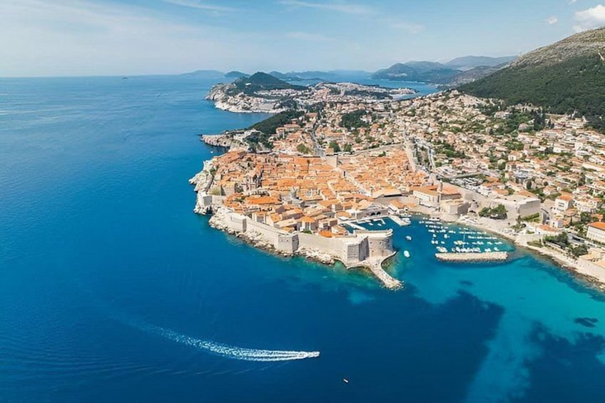 A coastal town with a historic fort, clear blue waters, and a mountainous backdrop. 5