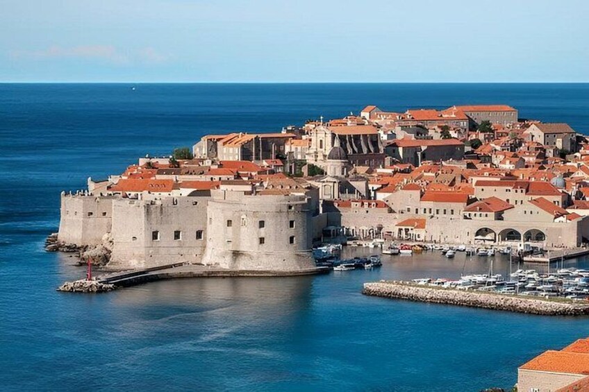 A coastal city with a prominent fortress, a harbor with boats, and a clear blue sky. 3