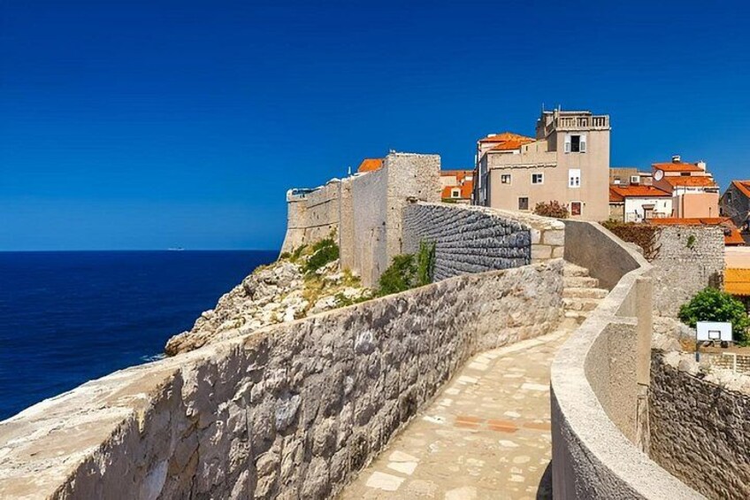 A coastal town with a historic stone wall, buildings with red-tiled roofs, and a clear blue sky. 4