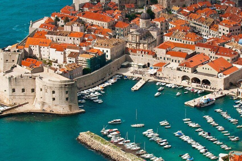 A coastal city with historic architecture, a fortified castle, and a marina with numerous boats. 2