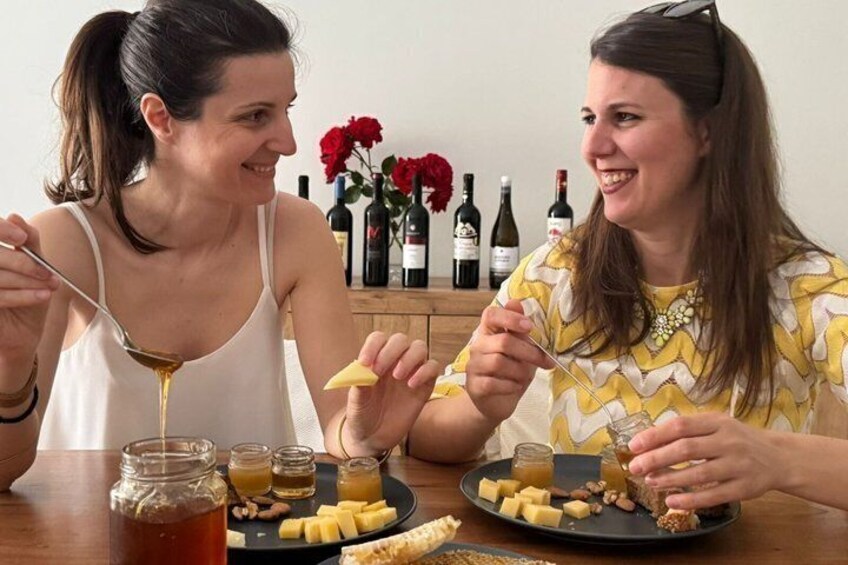 Two people eating at a table with cheese, honey, and wine bottles in the background. 4