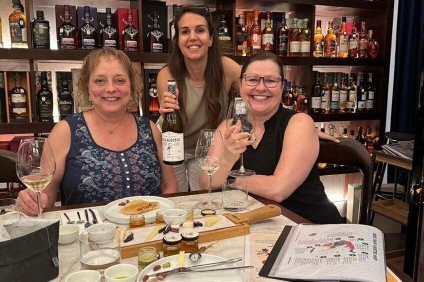 Three people at a table with wine glasses, a menu, and a bottle of wine. 2