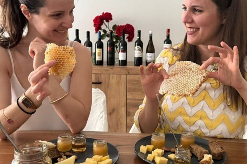 Two people examining honeycombs and a table with jars of honey, cheese, and bread. 3