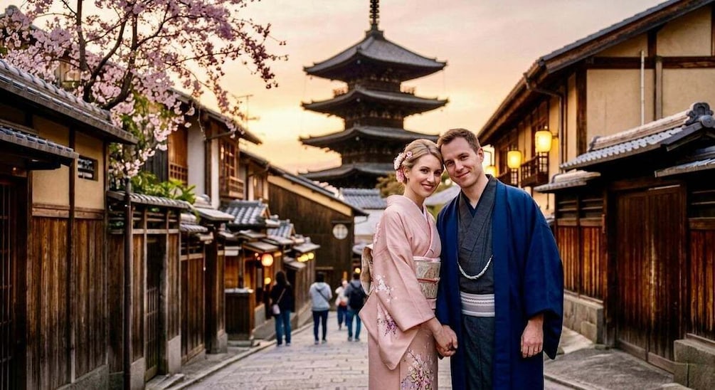 A couple in traditional attire standing in a narrow street with cherry blossoms and a pagoda in the background. 2