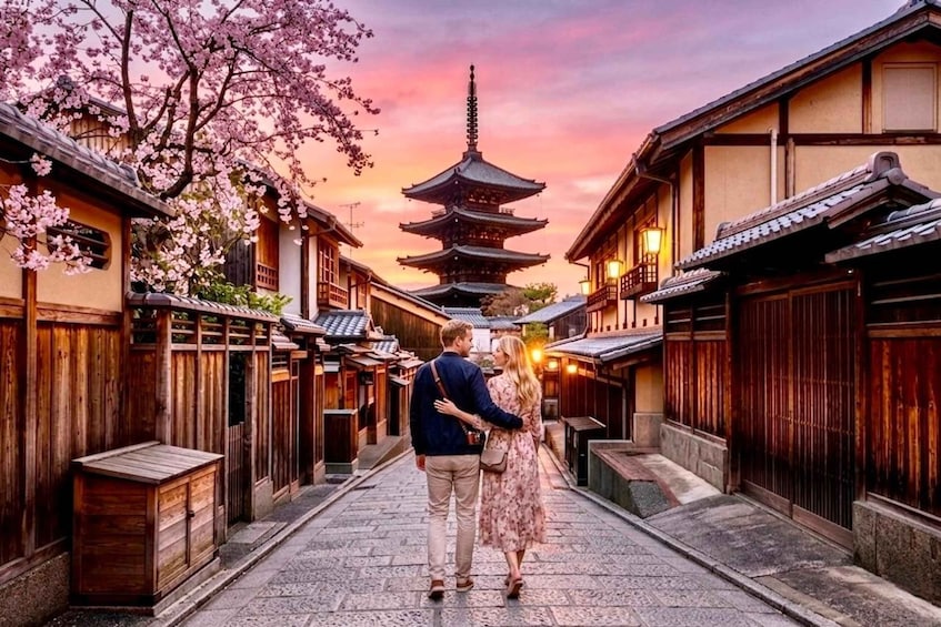 A couple walking down a traditional street with cherry blossoms and a pagoda in the background. 1