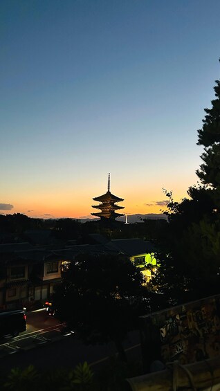 A pagoda silhouetted against a sunset sky, surrounded by buildings and trees. 2