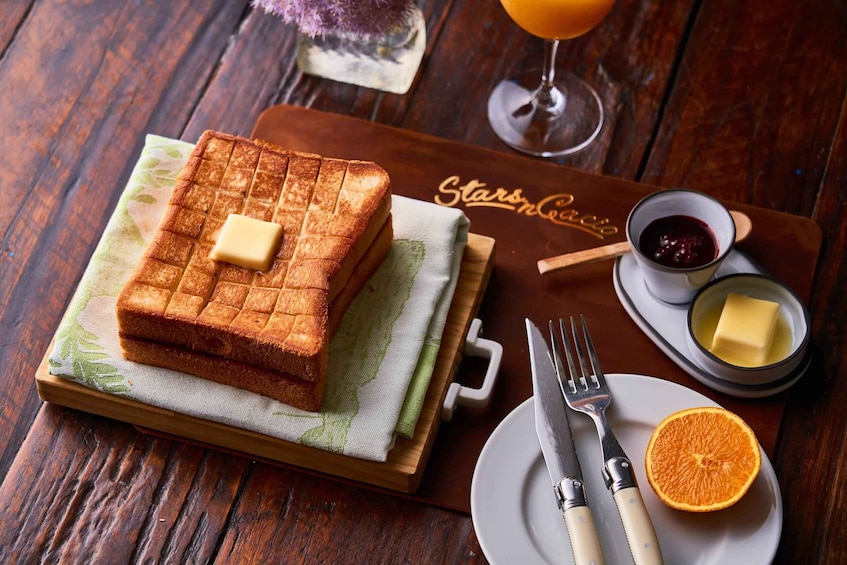 A breakfast setting with a waffle, butter, jam, and orange on a wooden table. 5
