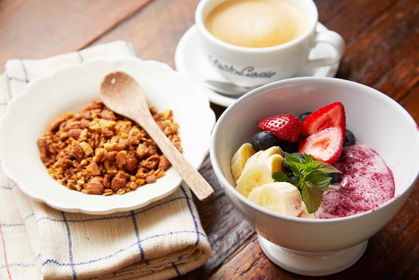 A bowl of granola with a wooden spoon, a cup of coffee, and a bowl of fruit and yogurt. 4