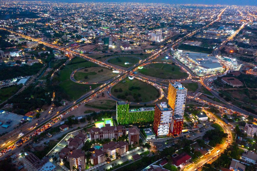 A cityscape at night with a prominent roundabout, illuminated buildings, and a dense network of roads. 2