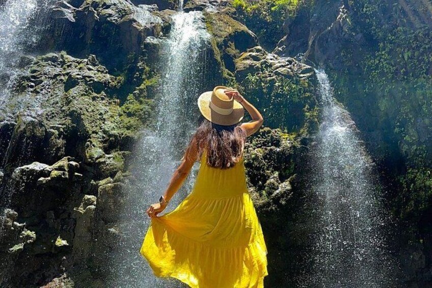 A person in a yellow dress and hat standing near a waterfall. 5