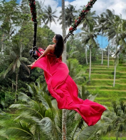 A person in a red dress swinging on a rope amidst lush greenery and palm trees. 5