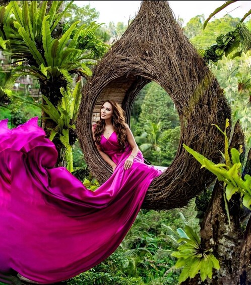 A person in a pink dress sitting in a hanging wicker chair amidst lush greenery. 4