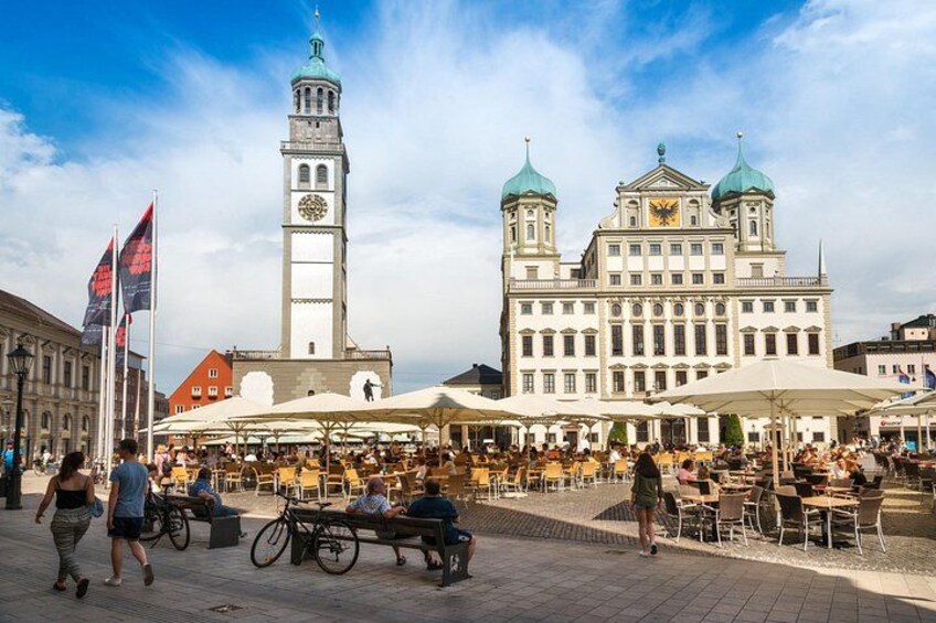 Une place publique abritant un bâtiment historique, une tour de l’horloge et des espaces de détente en plein air. 4