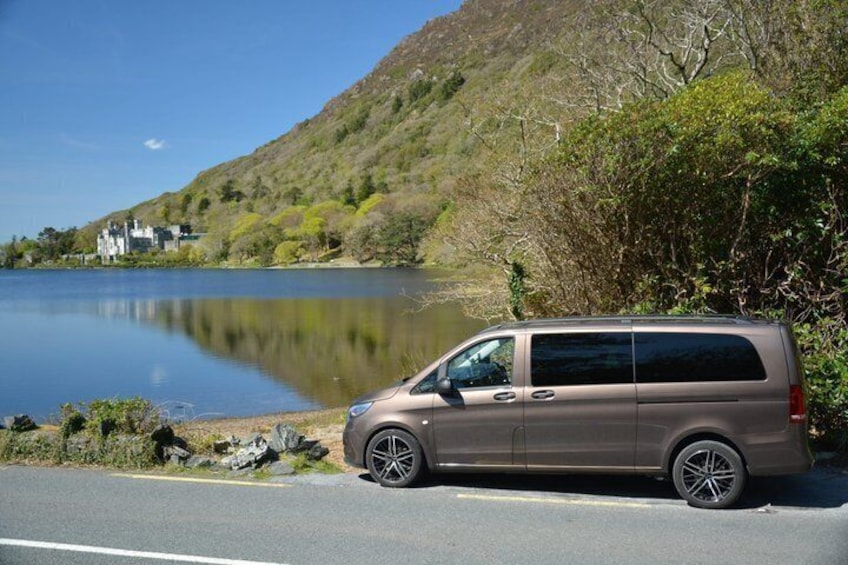 A brown van parked by a lake with a house in the background. 3