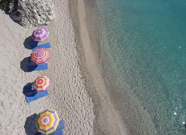 A beach with four colorful umbrellas and blue lounge chairs. 2
