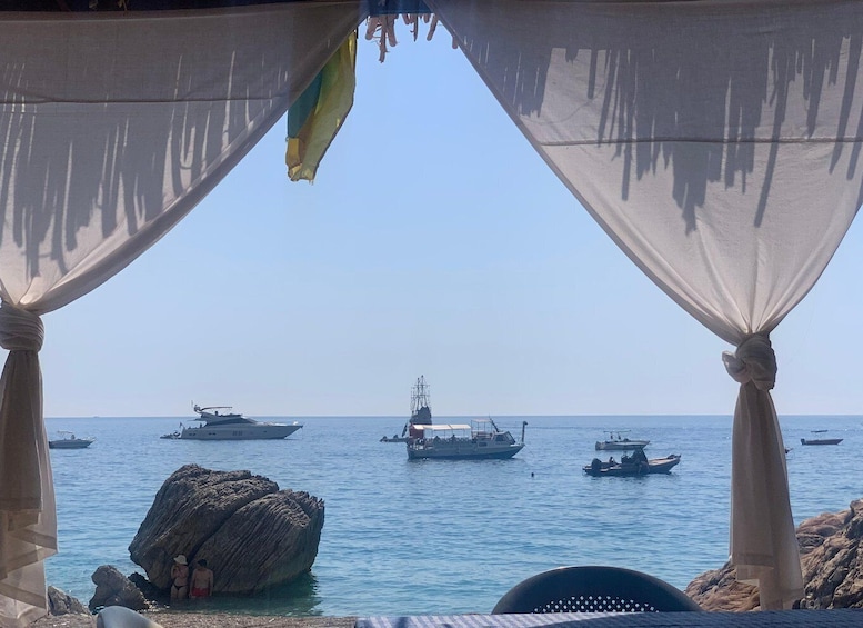A beach with a rocky outcrop and a view of the sea with several boats. 1
