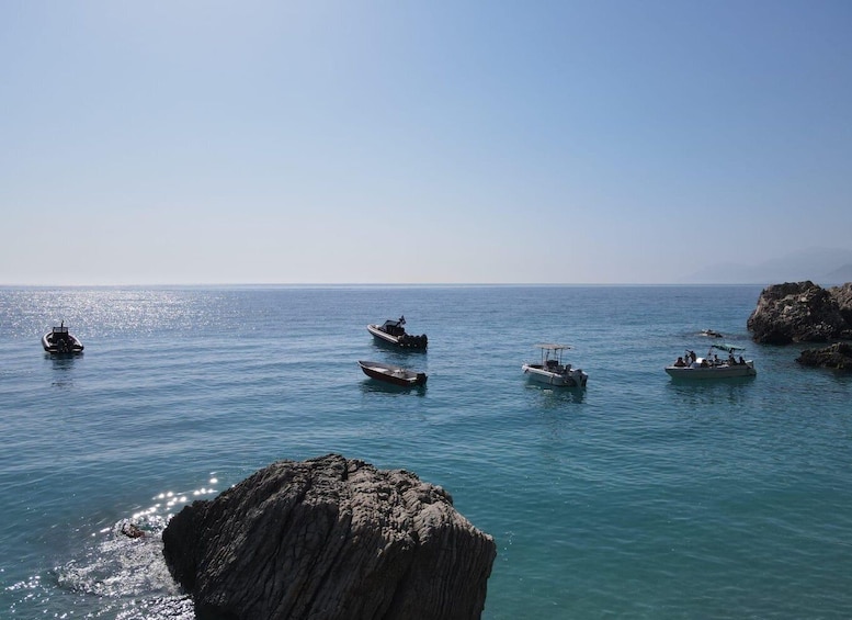 A calm sea with several boats anchored near rocky outcrops. 4