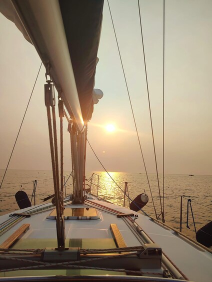 A sailboat's deck with rigging and a view of the sunset over the water. 5