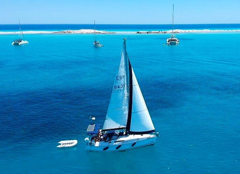 A sailboat with the registration ESP 8439 sailing on turquoise waters with other boats in the background. 1