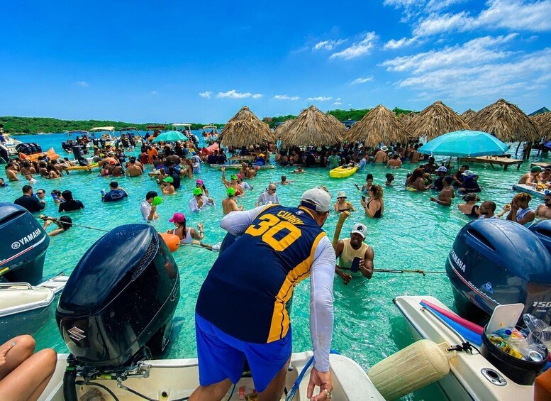 A crowded beach with people swimming and sunbathing, thatched umbrellas, and boats with Yamaha outboard motors. 4