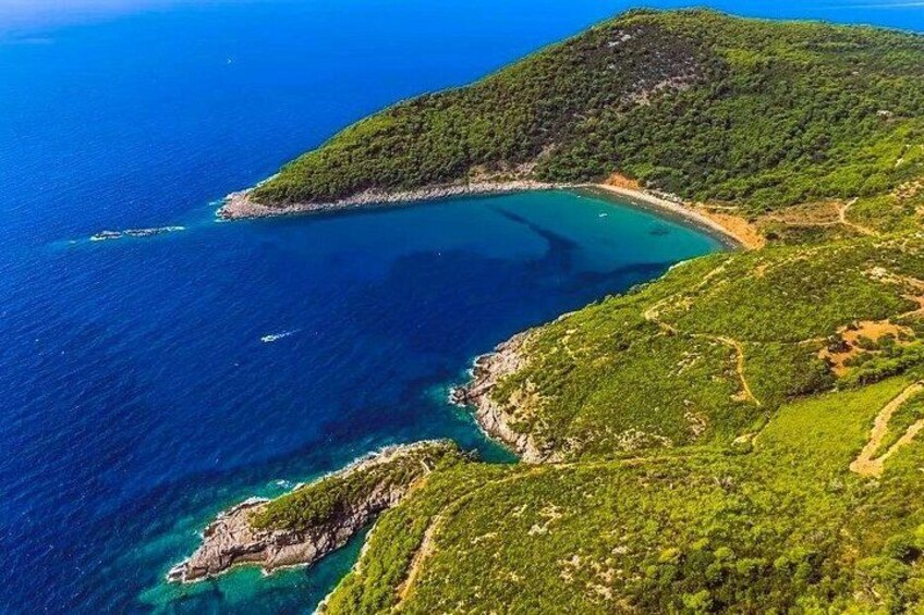 A coastal landscape with a clear blue sea, a green hill, and a rocky coastline. 3