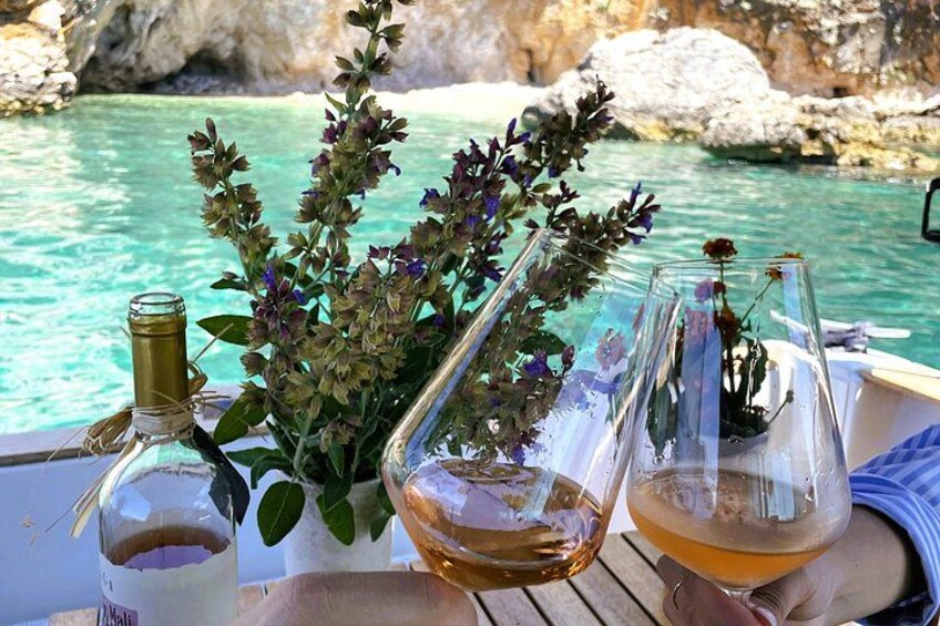 A boat with a bottle of white wine, a glass with a flower arrangement, and a glass of wine by a turquoise sea. 5