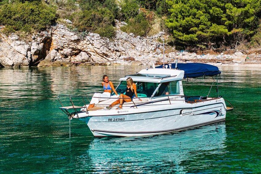 A boat with two people on it, anchored near a rocky shore with trees. 1
