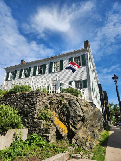 A historic building with green shutters, a stone wall, and a flag. 3