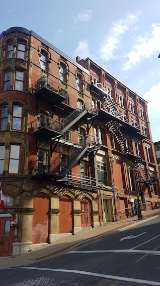 A red brick building with multiple fire escapes and a street in front. 4