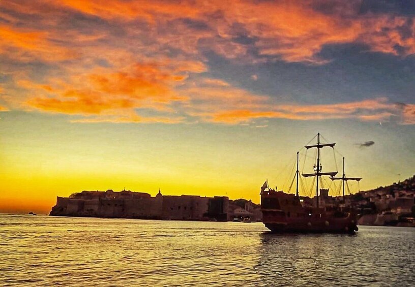 A sunset over a harbor with a ship and a historic fort. 1