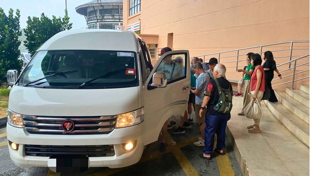 A white van parked at a curb with people boarding it. 1