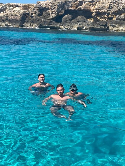 Two people swimming in clear blue water with rocky cliffs in the background. 2