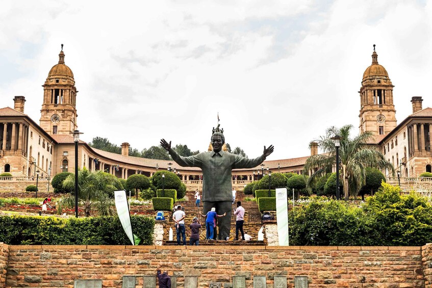 A large statue with outstretched arms in front of a historic building with two towers. 1