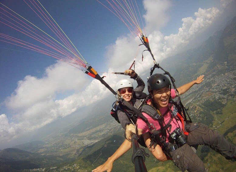 Two people paragliding with colorful parachute lines against a mountainous landscape. 4