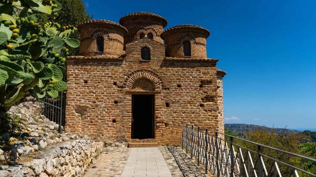 A stone building with a central archway and three domed structures on top. 5