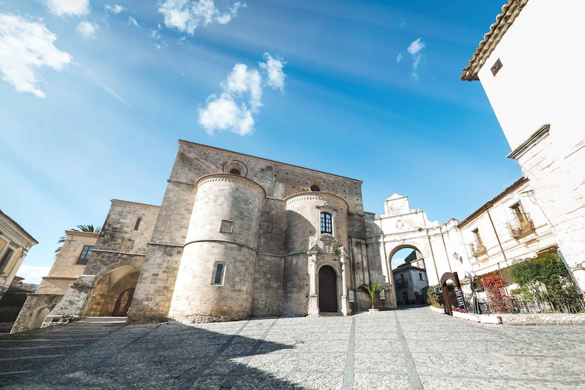 A historic stone building with a large arched entrance, a central tower, and a cobblestone courtyard. 3