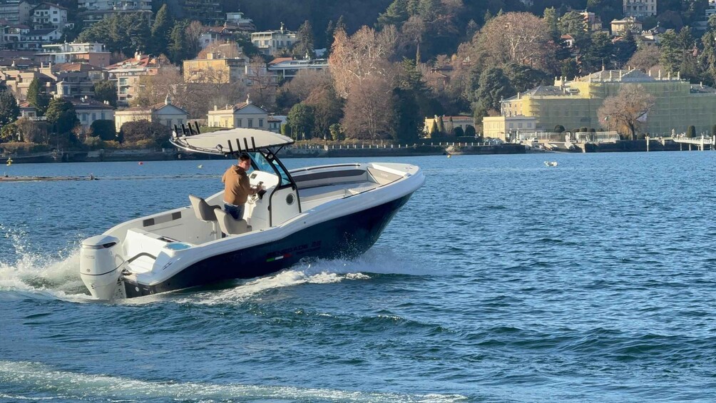 A speedboat with a single occupant on a calm lake, surrounded by residential buildings and trees. 5