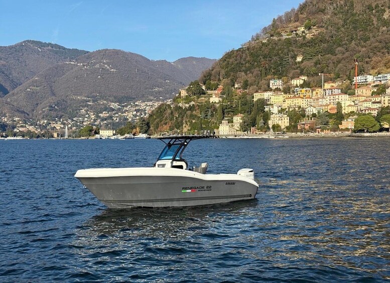 A white motorboat named 'Reneade 22' on calm water with a backdrop of a mountainous coastline and a densely built town. 2