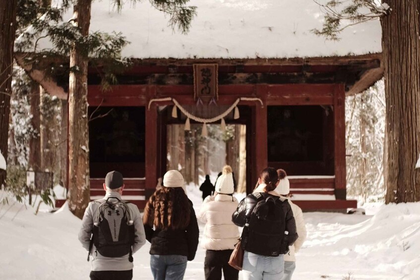 A group of people walking towards a traditional red building in a snowy forest. 1
