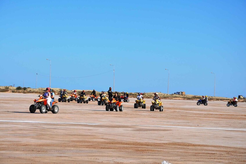 A group of people riding quad bikes on a flat, barren landscape with clear skies. 3