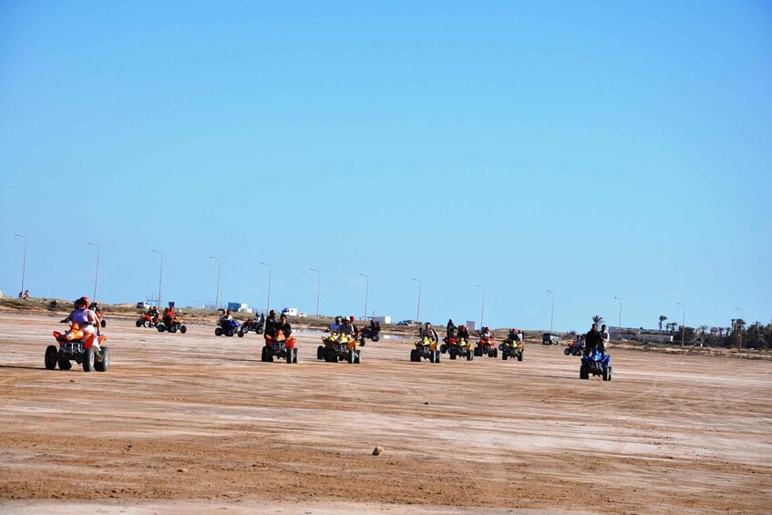 A group of people riding quad bikes on a dirt track. 5