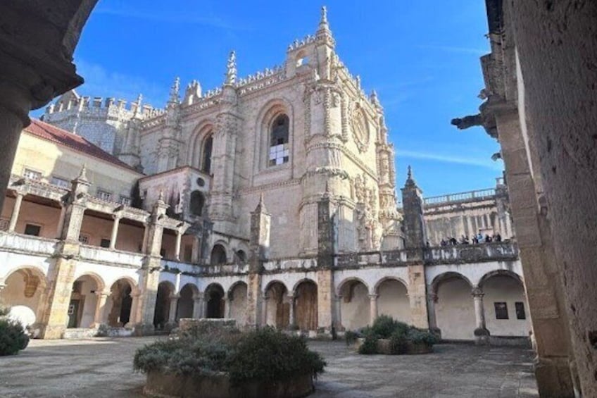 A historic cathedral with intricate architecture, a courtyard with arches, and a clear blue sky. 1