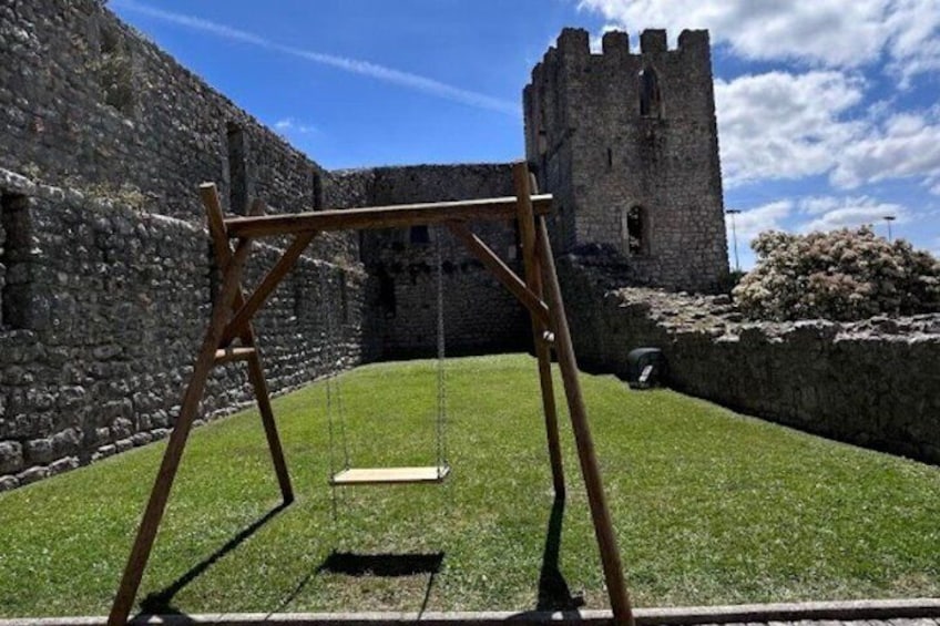 A wooden swing set in front of a stone wall and a castle. 2