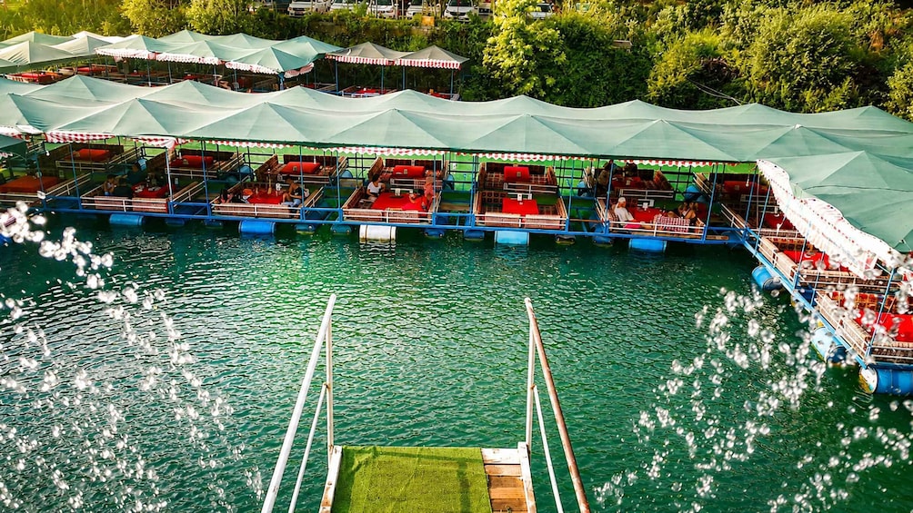 A floating restaurant with multiple dining areas on the water, surrounded by green canopies. 2