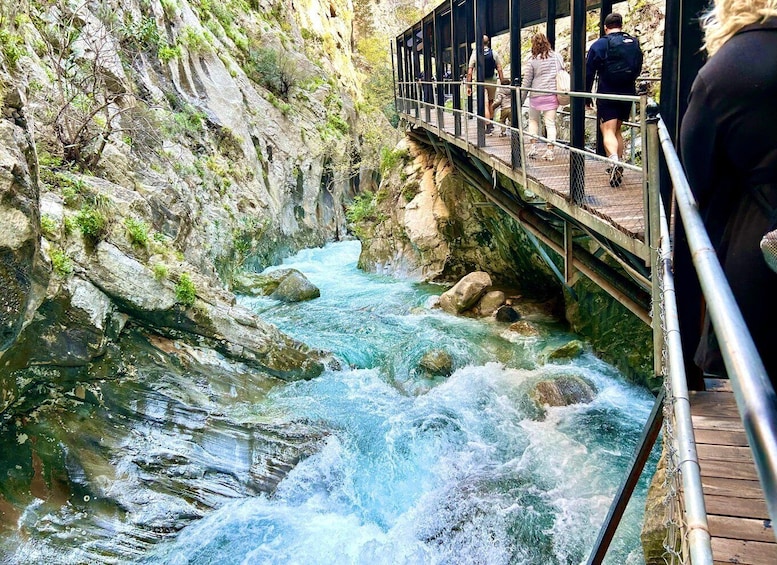 A wooden bridge over a fast-flowing river with rocky cliffs on either side. 5